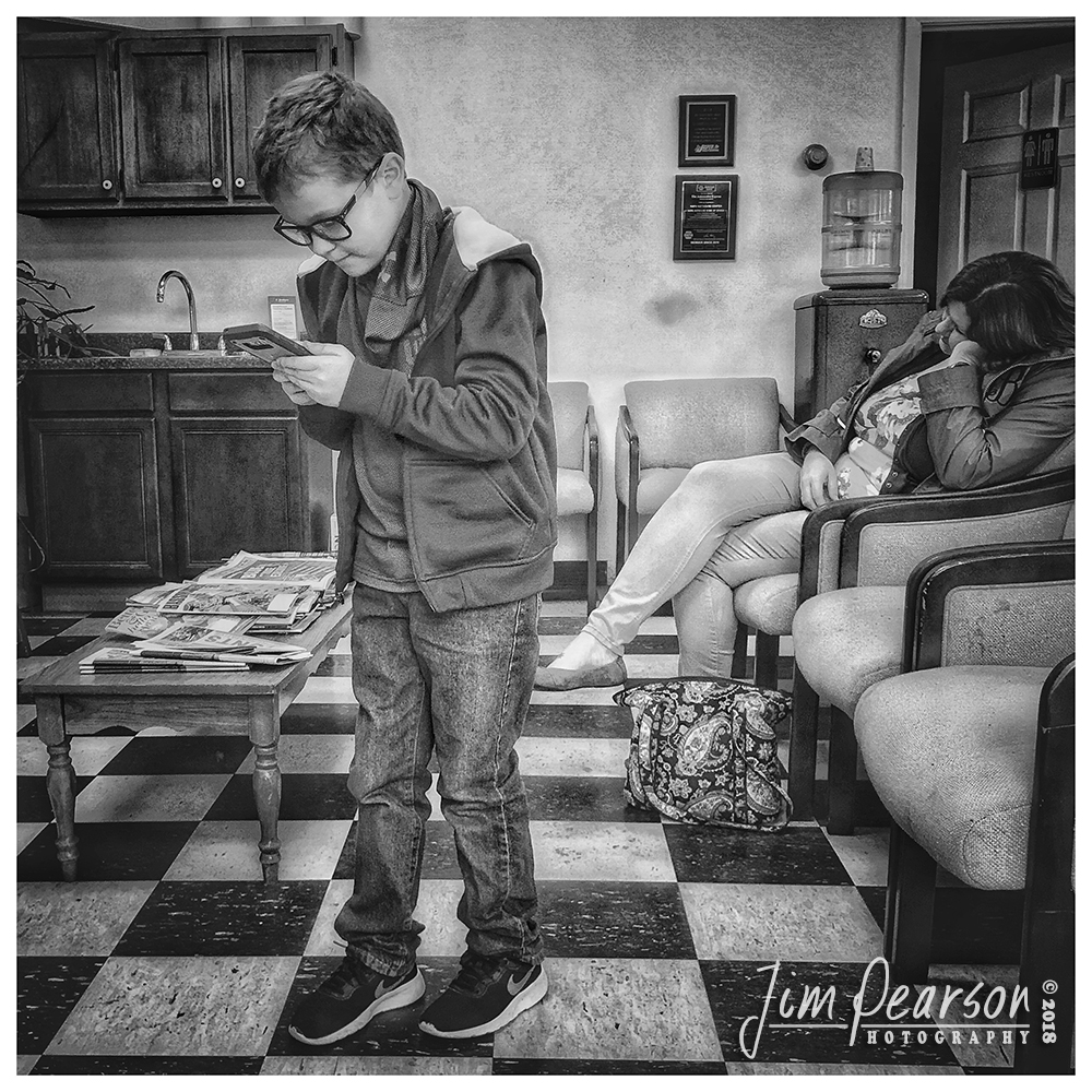November 1, 2018 - Day 367 - iPhone 7 Plus Daily B/W Photo Challenge - The Waiting Game - This young boy was playing a game on his mom's phone, that seemed to require him to get up and move around a little, as they were waiting for their car to get an oil change. Sometimes photos and puns just happen!