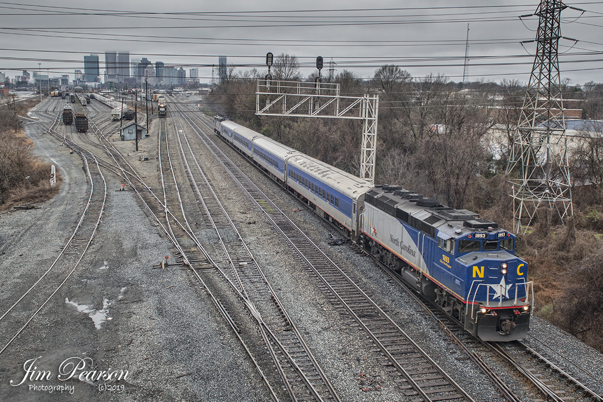 January 13, 2019 - NC Piedmont commuter train 74, with locomotive 1893, City of Burlington, leading, heads north out of the NS Charlotte Yard at Charlotte, NC bound for Raleigh, NC under stormy skies. According a 2011 press release from NCDOT, The North Carolina Department of Transportation's Rail Division commissioned the #1893 "City of Burlington" commuter locomotive into service for the use in their daily Piedmont passenger train service on December 15th, 2011. The then newly-refurbished locomotive replaced the locomotive damaged in a crash in Mebane in 2010. The #1893 "City of Burlington" is painted in the NCDOT Piedmont paint scheme, which incorporates the colors and symbols of North Carolina's state flag. NCDOT names its locomotives for the cities along its passenger rail corridor.  Each locomotive's number corresponds to the incorporation or charter date of the city after which it is named. - #jimstrainphotos #northcarolinarailroads #trains #nikond800 #railroad #railroads #train #railways #railway #NC #NCrailroads
