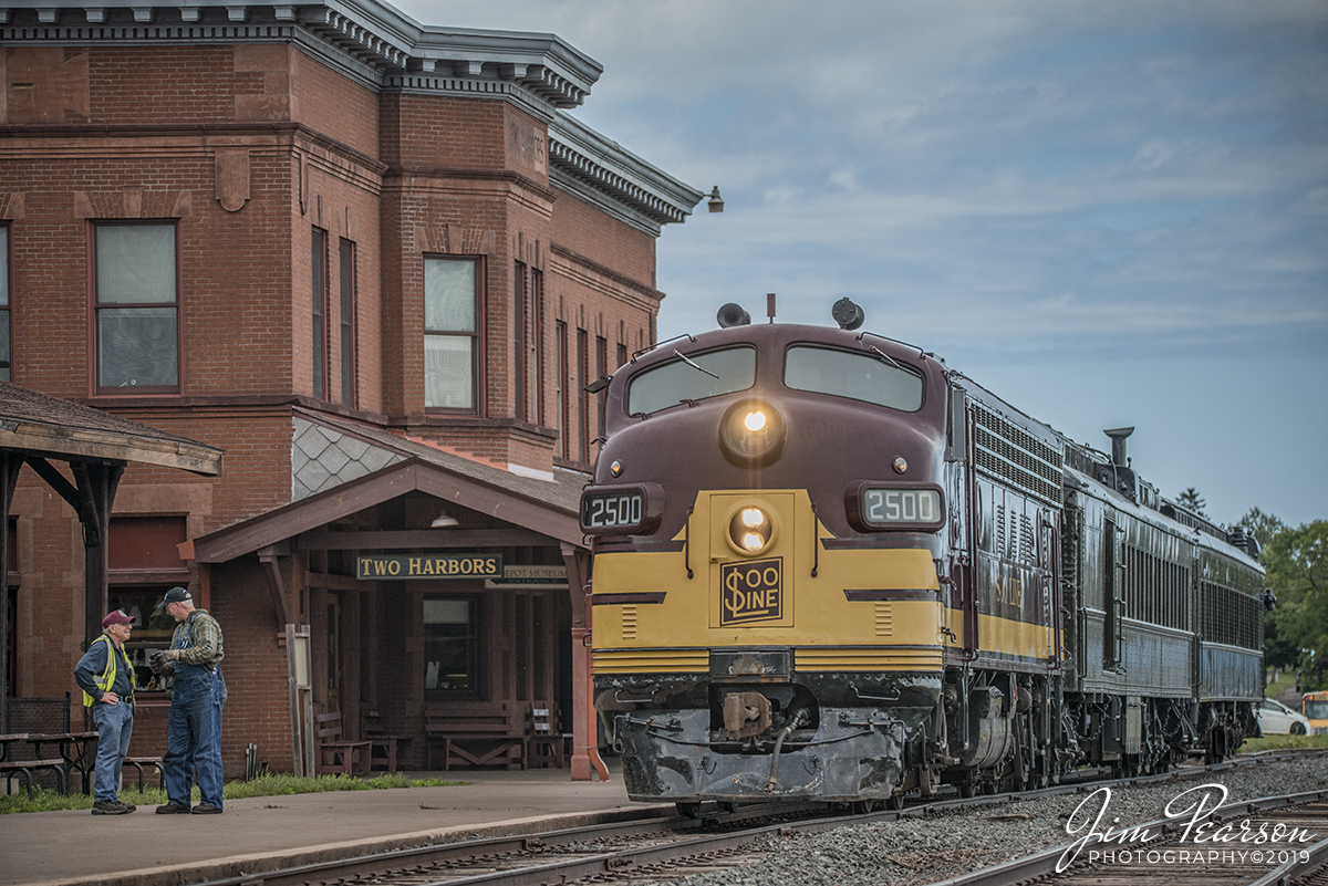 September 6, 2019 - Soo Line/Wisconsin Central FP7 Number 2500-A sits in the station at Two Harbors, Minnesota  as the CN yard man and the engineer from our photo excursion train talk on the platform. Everyone from the photo excursion passenger train on the North Shore Scenic Railroad with are off the train shooting their photos of the train set, as we all wait for permission into the CN yard at Two Harbors so our train can be turned and head back to Duluth, Minnesota. 

According to Wikipedia: With steam operations on North American Railroads being converted to diesel operations, Electro-Motive, along with other locomotive builders, began building demonstrator units to be tested by various railroads. Electro-Motive built a set of three FP7 units, 7001 (A-unit) and 7002 & 7003 (B-units). In November 1949, Canadian Pacific Railway tested these units. Canadian Pacific owned most of the Soo Line, and after testing the three demonstrator units, they were sent to the Soo Line.

In April 1950, Soo Line ran the set from Minneapolis, MN to Portal, ND then Duluth, MN to Winnipeg. 7001 hosted the United Kingdom's Duke of Windsor, the former King Edward VIII, in its cab through North Dakota. Soo Line was so impressed with the set, that it purchased them for use on Wisconsin Central. In May 1950, they were delivered as WC 2500-A, 2500-B, and 2501-B.

WC 2500-A often pulled Soo's Laker from Chicago to Duluth. Although numbered as Wisconsin Central, 2500 was painted in Soo Line's maroon and gold scheme. In 1960 Wisconsin Central became part of the Soo Line, and 2500 was repainted into the red and gray Soo Line scheme. When passenger service was discontinued in the 1960s, 2500 was used to pull freight trains.