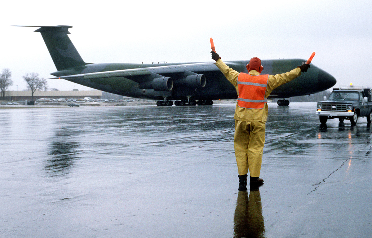 Blast From The Past - April 1, 1984 - A ground crewman wearing foul weather gear uses flashlights to signal a pilot as he maneuvers a C-5 Galaxy aircraft into position on the flight line during Exercise GLOBAL SHIELD '84 at Offutt Air Force Base, NE. - USAF Photo by SSgt. James R. Pearson