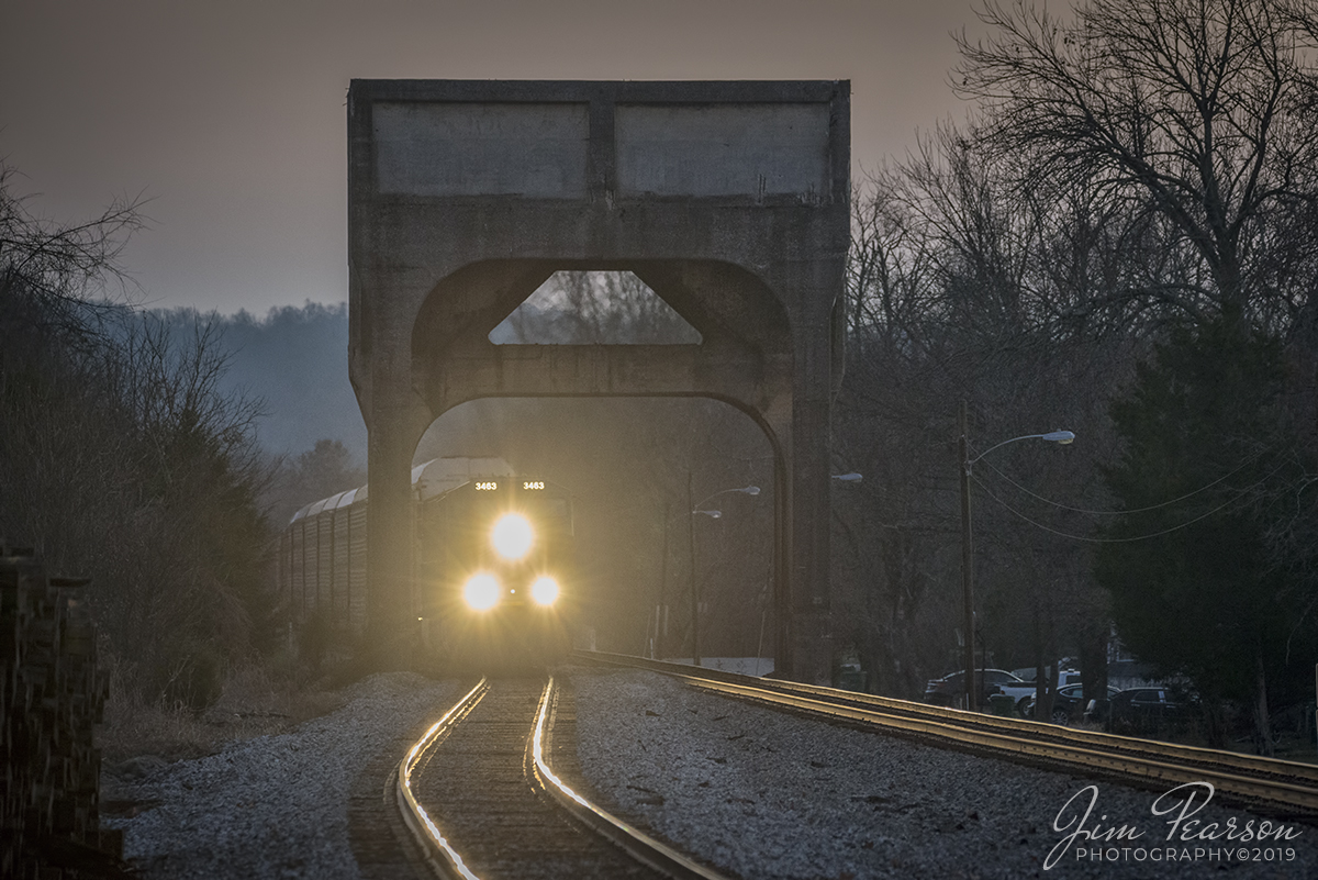 December 7, 2019 - As the last light of the day fades, CSXT 3463 leads CSX Q224 under the old coaling tower at Lebanon Junction, Kentucky as it heads north on the Mainline Subdivision (Short Line). 

According to Wikipedia: Lebanon Junction sprang into existence from a railroad switching point that split Louisville and Nashville Railroad (now CSX Transportation) traffic off the mainline to the Lebanon branch that ended in Lebanon, Kentucky. This branch was completed no later than March 8, 1858, and the town grew out of a need for railroad workers to man the terminal and switching station.

A coaling tower, coal stage or coaling station is a facility used to load coal as fuel into railway steam locomotives. Coaling towers were often sited at motive power depots or locomotive maintenance shops.

Coaling towers were constructed of wood, steel-reinforced concrete, or steel. In almost all cases coaling stations used a gravity fed method, with one or more large storage bunkers for the coal elevated on columns above the railway tracks, from which the coal could be released to slide down a chute into the waiting locomotive's coal storage area. The method of lifting the bulk coal into the storage bin varied. The coal usually was dropped from a hopper car into a pit below tracks adjacent to the tower. From the pit a conveyor-type system used a chain of motor-driven buckets to raise the coal to the top of the tower where it would be dumped into the storage bin; a skip-hoist system lifted a single large bin for the same purpose. Some facilities lifted entire railway coal trucks or wagons. Sanding pipes were often mounted on coaling towers to allow simultaneous replenishment of a locomotive's sand box.

As railroads transitioned from the use of steam locomotives to the use of diesel locomotives in the 1950s the need for coaling towers ended. Many reinforced concrete towers remain in place if they do not interfere with operations due to the high cost of demolition incurred with these massive structures.