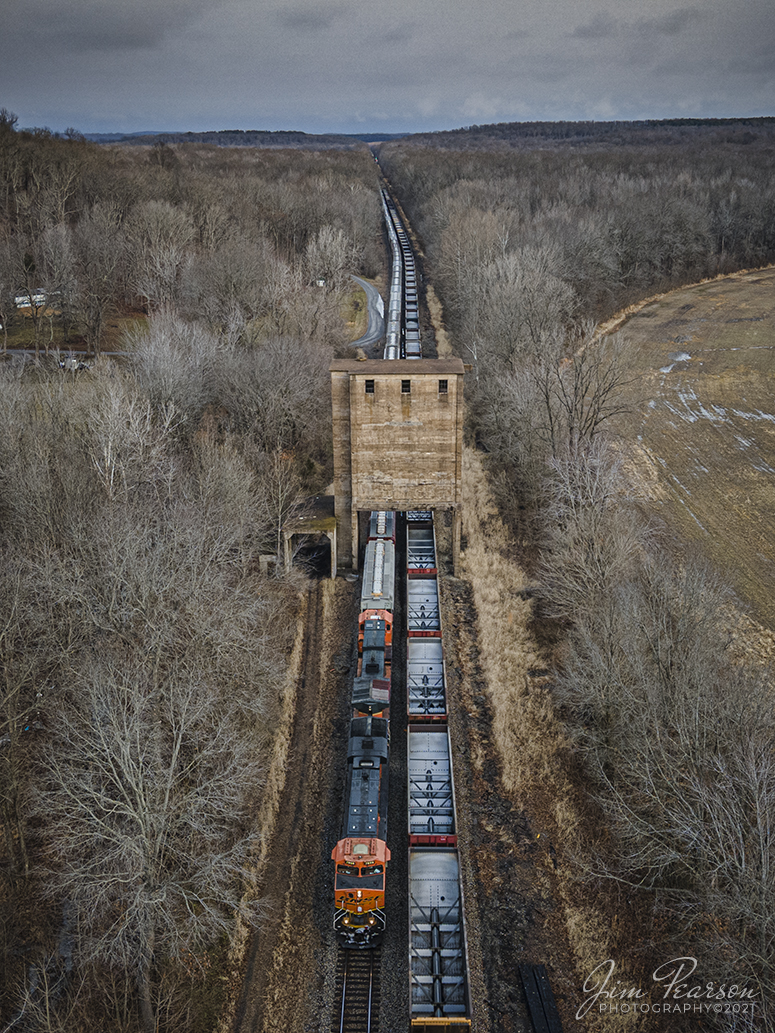 BNSF and CN meet at Reevesville, Illinois

On January 2nd, 2020 a empty BNSF grain train sits in the siding at Reevesville, Illinois as a empty CN coal train heads north, on CNs Bluford Subdivision, under the old Illinois Central Steam Train coaling tower.

According to Wikipedia: A coaling tower, coal stage or coaling station was a facility used to load coal as fuel into railway steam locomotives. Coaling towers were often sited at motive power depots or locomotive maintenance shops.

Coaling towers were constructed of wood, steel-reinforced concrete, or steel. In almost all cases coaling stations used a gravity fed method, with one or more large storage bunkers for the coal elevated on columns above the railway tracks, from which the coal could be released to slide down a chute into the waiting locomotives coal storage area. The method of lifting the bulk coal into the storage bin varied. The coal usually was dropped from a hopper car into a pit below tracks adjacent to the tower. From the pit a conveyor-type system used a chain of motor-driven buckets to raise the coal to the top of the tower where it would be dumped into the storage bin; a skip-hoist system lifted a single large bin for the same purpose. Some facilities lifted entire railway coal trucks or wagons. Sanding pipes were often mounted on coaling towers to allow simultaneous replenishment of a locomotives sand box.

As railroads transitioned from the use of steam locomotives to the use of diesel locomotives in the 1950s the need for coaling towers ended. Many reinforced concrete towers remain in place if they do not interfere with operations due to the high cost of demolition incurred with these massive structures.

Tech Info: DJI Mavic Air 2 Drone, JPG, 4.5mm (24mm equivalent lens) f/2.8, 1/120, ISO 400.