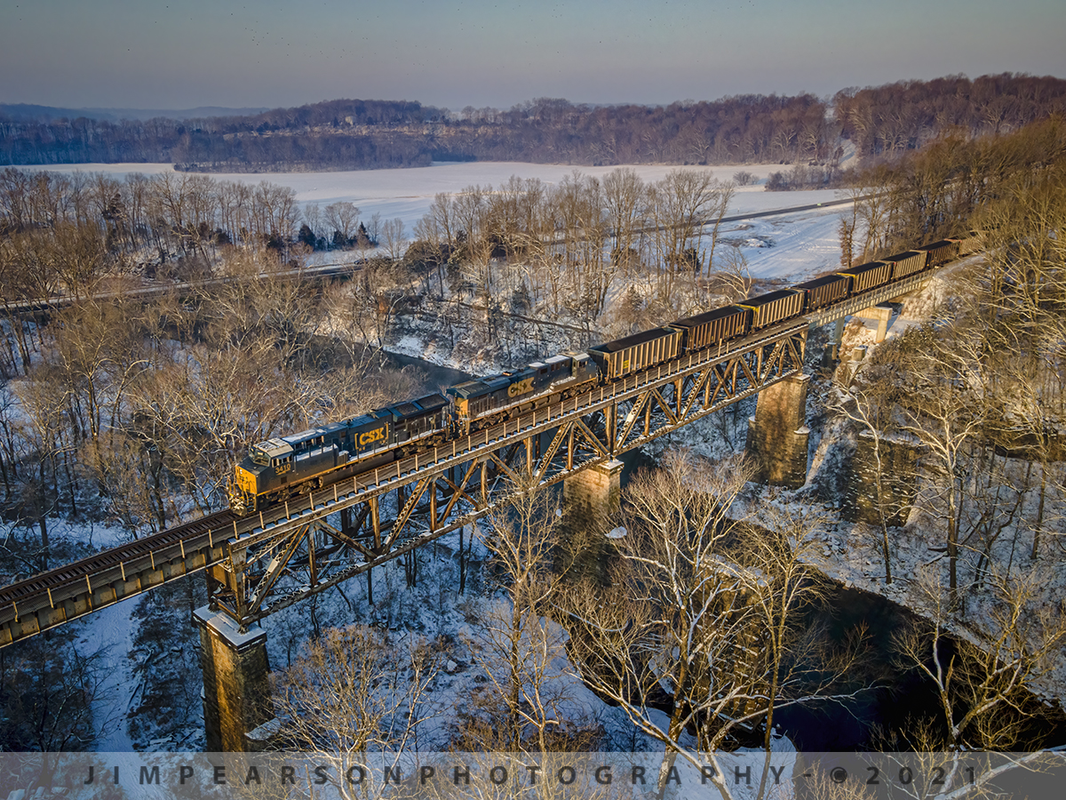First light, first train!

I was afraid I'd miss this loaded coal train CSX N302 at first light on the Red River bridge at Adams, Tennessee as it made its way south on the Henderson Subdivision.

I left my house at about 5:30am, much earlier than I'm accustomed to getting out, but I was meeting fellow railfan Cooper Smith at 7am at Guthrie, Kentucky and we were to meet at the CSX yard in Guthrie to do a full day of railfanning in the snow.

After stopping to shoot the sun popping over the horizon just north of Trenton, Ky I got back in my nice and toasty SUV after getting my shot in the cold 14 degree weather and headed on south to meet up with Cooper. It was about this time I found out that he was running late and that there was a loaded coal train just ahead of me headed south.

This was just after the last big snowfall that swept through the region the day before and even though the Kentucky and Tennessee road crews had do a great job of plowing US 41, which follows the Henderson Subdivision, there was still ice on the roads to contend with so I was worried that I wouldn't make it to this spot and get the drone up before the train got there, but as you can tell, lady luck was smiling in my direction!

I arrived at this spot probably about 10 minutes before the train on February 19th, 2021 and the sun was just above the tree line here and was sending that beautiful early morning golden light, raking across the bare trees. A great start to a great day of being trackside, even if it was real early and went till after dark! We both came back with some great shots!

Tech Info: DJI Mavic Air 2 Drone, RAW, 4.5mm (24mm equivalent lens) f/2.8, 1/500, ISO 100.