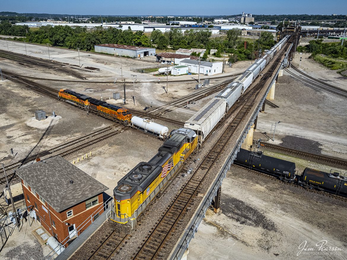 Union Pacific 8897 brings up rear as DPU on a grain train as it heads across Santa Fe Junction on the Kansas City Terminal Railroad (KCT) High Line, while BNSF 7767 and 3947 lead a westbound train past Tower #3 on June 30th, 2022.

Santa Fe Junction sees on average over 100 trains a day and it hosts the double decked railroad (ATSF Double Deck Railroad) bridge that crosses the Kansas River into Missouri, a triple crossing in addition to Tower 3, which is used by maintenance of way these days. The junction is partly in Missouri and Kansas and sees BNSF, UP, KCT, Amtrak, KCS, NS and CP traffic, from what I saw during my visit.

The Kansas City Terminal Railway Company (KCT) is a Class III railroad located in Kansas City, Missouri and Kansas City, Kansas. KCT serves as a terminal railroad for its five Class I railroad owners (Union Pacific, BNSF, Kansas City Southern, Norfolk Southern and Canadian Pacific).  Amtrak also operates over the KCT providing passenger service to and from Union Station. Currently the second largest rail hub in the United States, KCT owns and dispatches 95 miles of track spanning Missouri and Kansas.

According to the website railfanguides.us Santa Fe Junction Interlocking is easily the busiest location for trains in Kansas City and trains from any of the five railroads which jointly own KCT can be seen here. Tower #3 was closed in 1969 when a central dispatching center replaced it and all the other towers KCT had at the time.

The black bridge is KCTs double deck, double track crossing of the Kansas River. The odd-looking silver towers on the bridge are lift mechanisms to raise the bridge in the event of flooding and are not connected most of the time. The upper deck line was primarily used by passenger trains from UP and Rock Island, moving to and from Kansas through the KC Union Station. Today primarily freight trains use this bridge. 

The tracks through the junction have been reduced or changed around over the years, but the area remains one of KCs Busiest locations.

Tech Info: DJI Mavic Air 2S Drone, RAW, 22mm, f/2.8, 1/2000, ISO 100.

#trainphotography #railroadphotography #trains #railways #dronephotography #trainphotographer #railroadphotographer #jimpearsonphotography