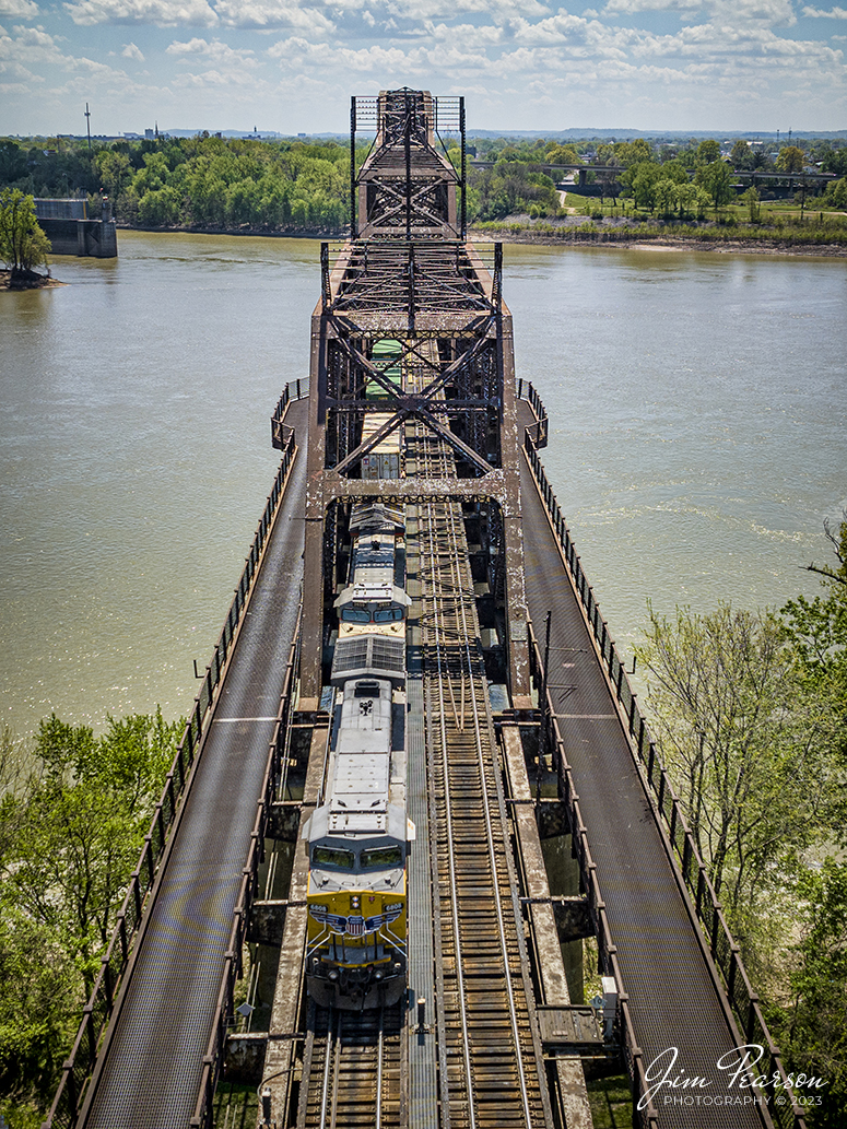 Union Pacific 6808 and 2659 lead Norfolk Southern 224 over the K&I bridge out of Louisville, Kentucky as they head west over the Ohio River into New Albany, Indiana on the NS Southern East District on April 15th, 2023.

According to Wikipedia: The Kentucky & Indiana Bridge is one of the first multi modal bridges to cross the Ohio River. It is for both railway and common roadway purposes together. By federal, state, and local law railway and streetcar, wagon-way, and pedestrian modes of travel were intended by the City of New Albany, City of Louisville, State of Kentucky, State of Indiana, the United States Congress, and the bridge owners. 

The K & I Bridge connects Louisville, Kentucky to New Albany, Indiana. Constructed from 1881 to 1885 by the Kentucky and Indiana Bridge Company, the original K&I Bridge opened in 1886. It included a single standard gauge track and two wagon ways, allowing wagons and other animal powered vehicles to cross the Ohio River by a method other than ferry for the first time. At the time motorized vehicles were virtually nonexistent. 

The K&I Bridge company also owned a ferry boat operation during both the 1st and 2nd bridge; eventually that operation was sold as the bridge's success largely outmoded boat usage.

In 1910 the bridge company was renamed the Kentucky & Indiana Terminal Railroad Co. From 1910 to 1912, a new, heavier bridge was built on new piers just upstream from the original one, after which the old bridge was demolished. The new bridge was double tracked to handle increasingly heavier train and now automobile traffic, eventually receiving the U.S. 31W designation.

The bridge also featured a rotating swing span opening for the passage of ships in high water. The bridge was only opened four times, twice for testing in 1913 and 1915, then in 1916 for the passage of the steamer "Tarascon" and in 1920 for passage of the Australian convict ship "Success". In 1948 it refused opening of the span for passage of the steamer "Gordon C. Greene" citing inconvenience and costs of cutting power and communication lines, an action for which K&I and LG&E both paid damages to that ship's company. In 1955 the K&I sought and received permission to permanently tie down the swing span from the Corps of Engineers. In 1952, the creosoted wood block roadways of the second bridge were eliminated and replaced by a steel gridwork roadway.

On February 1, 1979, an overweight dump truck caused a small segment of the steel grate roadway on the bridge to sag about 1 foot (0.30 m). A quick survey promised to reopen the roadway, but automotive traffic was banned thereafter by the railroad.

Tech Info: DJI Mavic 3 Classic Drone, RAW, 24mm, f/2.8, 1/2500 sec, ISO 130.

#trainphotography #railroadphotography #trains #railways #dronephotography #trainphotographer #railroadphotographer #jimpearsonphotography #kentuckytrains #mavic3classic #drones #trainsfromtheair #trainsfromadrone #LouisvilleKy #K&IBridge #UnionPacific #NS #norfolksouthern
