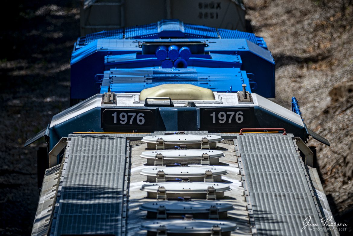 The newly released CSX Heritage series locomotive, 1976, Conrail Quality unit, pokes its nose above the train as it runs south as the DPU on CSX M513, at Adams, Tennessee on the Henderson Subdivision, on July 31st, 2023. 

DPU  Stands for Distributed Power Unit, which is a locomotive set capable of remote-control operation in conjunction with locomotive units at the train's head end. DPUs are placed in the middle or at the rear of heavy trains (such as coal, grain, soda ash and even manifest) to help climb steep grades.

According to Wikipedia: Conrail (reporting mark CR), formally the Consolidated Rail Corporation, was the primary Class I railroad in the Northeastern United States between 1976 and 1999. The trade name Conrail is a portmanteau based on the company's legal name. It continues to do business as an asset management and network services provider in three Shared Assets Areas that were excluded from the division of its operations during its acquisition by CSX Corporation and the Norfolk Southern Railway.

The federal government created Conrail to take over the potentially profitable lines of multiple bankrupt carriers, including the Penn Central Transportation Company and Erie Lackawanna Railway. After railroad regulations were lifted by the 4R Act and the Staggers Act, Conrail began to turn a profit in the 1980s and was privatized in 1987. The two remaining Class I railroads in the East, CSX Transportation, and the Norfolk Southern Railway (NS), agreed in 1997 to acquire the system and split it into two roughly equal parts (alongside three residual shared-assets areas), returning rail freight competition to the Northeast by essentially undoing the 1968 merger of the Pennsylvania Railroad and New York Central Railroad that created Penn Central. Following approval by the Surface Transportation Board, CSX and NS took control in August 1998, and on June 1, 1999, began operating their respective portions of Conrail.

Tech Info: Nikon D800, Sigma 150-600 @390mm, f/8, 1/1000, ISO 220.

#trainphotography #railroadphotography #trains #railways #dronephotography #trainphotographer #railroadphotographer #jimpearsonphotography #trains #csxt #mavic3classic #drones #trainsfromtheair #trainsfromadrone #CSXHeritageUnits