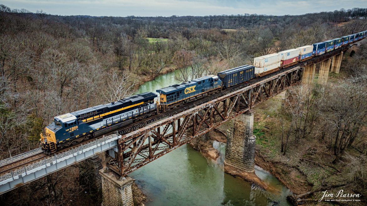 CSX Chesapeake & Ohio Heritage unit 1869 as it leads hot intermodal, CSX I026, across the Red River Bridge at Adam, Tennessee northbound on the Henderson Subdivision on February 27th, 2024.

According to the CSX Website: A locomotive commemorating the proud history of the Chesapeake and Ohio Railway has entered service as the fifth in the CSX heritage series celebrating the lines that came together to form the modern railroad.

Numbered CSX 1869 in honor of the year the C&O was formed in Virginia from several smaller railroads, the newest heritage locomotive sports a custom paint design that includes today’s CSX colors on the front of the engine and transitions to a paint scheme inspired by 1960s era C&O locomotives on the rear two-thirds.

The C&O Railway was a major line among North American freight and passenger railroads for nearly a century before becoming part of the Chessie System in 1972 and eventually merging into the modern CSX. In 1970, the C&O included more than 5,000 route miles of track stretching from Newport News, Virginia, to Chicago and the Great Lakes.

Designed and painted at CSXs locomotive shop in Waycross, Georgia, the C&O unit will join four other commemorative units in revenue service on CSXs 20,000-mile rail network.

The heritage series is reinforcing employee pride in the history of the railroad that continues to move the nation’s economy with safe, reliable, and sustainable rail-based transportation services.

Tech Info: DJI Mavic 3 Classic Drone, RAW, 22mm, f/2.8, 1/240, ISO 170.

#trainphotography #railroadphotography #trains #railways #jimpearsonphotography #trainphotographer #railroadphotographer #csxt #dronephoto #trainsfromadrone #trending