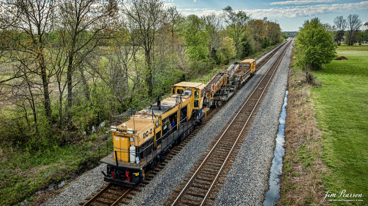 A Loram Badger Ditcher Machine, DC-2, heads north out of the siding at Crofton, Kentucky as W055-13, on April 12th, 2024, on the CSX Henderson Subdivision. 

According to their website: Loram’s Badger Ditcher is a self-propelled ditch cleaner that can move 1,000 tons of material every hour, excavating at up to 22 feet from the center of the track. The Loram ditch cleaner creates a properly sloped ditch that intercepts and diverts water away from the track. The ditcher’s high-speed, high-performance ditching wheel digs in and picks up mud and water. As the wheel digs the ditch, water begins to flow.

The Badger Ditcher helps manage, remedy, and prevent the damaging effects from a host of penetrating water sources, including direct precipitation, groundwater migration, springs and trapped water, saturation, and seepage. Ditch maintenance best practices using the Badger Ditcher lets railroads improve vital drainage for the subgrade, lower the water table, control run-off, and promote free flow from the ballast section that can extend the effective duration of undercutting and ballast cleaning cycles.

Tech Info: DJI Mavic 3 Classic Drone, RAW, 22mm, f/2.8, 1/1250, ISO 240.