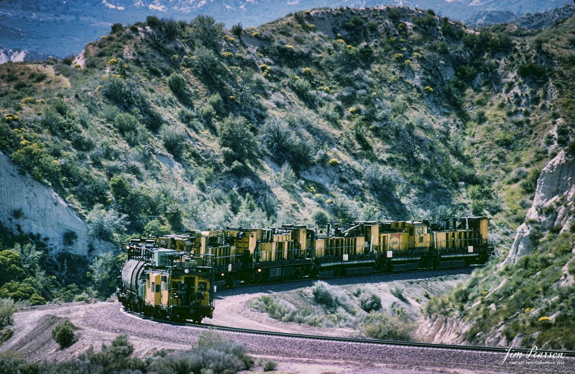 A Loram Rail grinder makes its way through the Cajon Pass in Southern California in April of 1995.

I spent a lot of years railfanning the pass between 1981 and 1995! It's a great place to catch trains and I've been back several times over the years since then.

In fact I'm headed back again this coming September for a week or so to see how much it has changed since I was last there several years ago. In fact, it was before I had a drone, so I'm really looking forward to railfanning from the air this next trip!

According to Wikipedia: Cajon Pass is a mountain pass between the San Bernardino Mountains to the east and the San Gabriel Mountains to the west in Southern California. Created by the movements of the San Andreas Fault, it has an elevation of 3,777 ft (1,151 m).[1] Located in the Mojave Desert, the pass is an important link from the Greater San Bernardino Area to the Victor Valley, and northeast to Las Vegas. The Cajon Pass area is on the Pacific Crest Trail.

Cajon Pass is at the head of Horsethief Canyon, traversed by California State Route 138 and railroad tracks owned by BNSF Railway and Union Pacific Railroad. Improvements in 1972 reduced the railroad's maximum elevation from about 3,829 to 3,777 feet (1,167 to 1,151 m) while reducing curvature. Interstate 15 does not traverse Cajon Pass, but rather the nearby Cajon Summit. The entire area, Cajon Pass and Cajon Summit, is often referred to as Cajon Pass, but a distinction is made between Cajon Pass and Cajon Summit.

Nikon F3 Camera, Nikon 300mm lens, f/stop and shutter speed not recorded