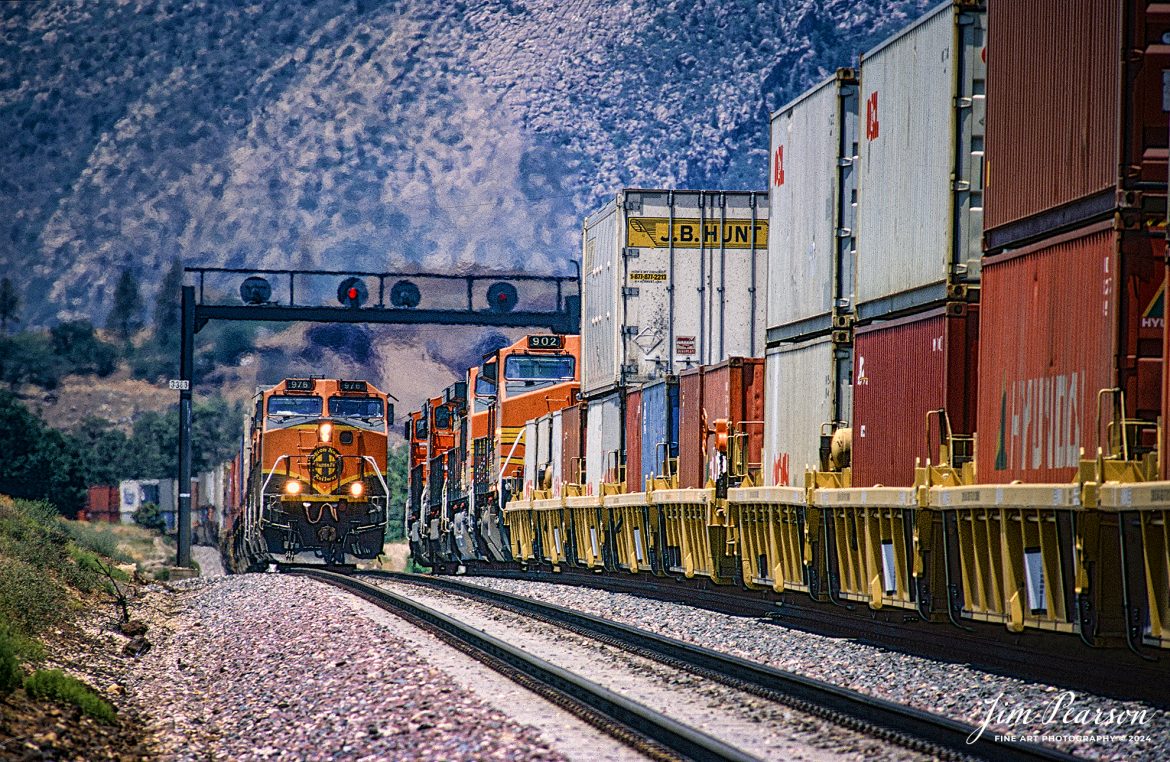 Eastbound and Westbound stack trains meet at the signal bridge at MP 336.3 on the Union Pacific’s Mojave Subdivision at Mojave, California in the mid-1990s.

According to Wikipedia, the Mojave Subdivision refers to a series of railway lines in California. The primary route crosses the Tehachapi Pass and features the Tehachapi Loop, connecting Bakersfield to the Mojave Desert. East of Mojave, the line splits with the Union Pacific Railroad portion continuing south to Palmdale and Colton over the Cajon Pass and the BNSF Railway owned segment running east to Barstow. Both companies generally share trackage rights across the lines.

The route over the Tehachapi Pass was constructed by the Southern Pacific Railroad as their main line south to the Colorado River. As part of their charter, the company was steadily building south in the San Joaquin Valley after having abandoned plans to do so via the coastal route. Built simultaneously to the Fresno Subdivision, the rail head reached Goshen in August 1872, Delano on July 14, 1873, Caliente on April 26, 1875, and Mojave on August 9, 1876. The completion of the line through the Soledad Canyon in 1876 provided the first link between Los Angeles and San Francisco via rail. The Victorville Cutoff was opened in 1967, and the Union Pacific's track over the Cajon Pass was built by the Los Angeles and Salt Lake Railroad.

The Atchison, Topeka and Santa Fe Railway had purchased the San Francisco and San Joaquin Valley Railroad in 1898, but the valley was isolated from their mainline which ran from Needles to Los Angeles and San Diego. After the Valley Division was opened in 1900, they negotiated with Southern Pacific for the right to run trains over the Tehachapi. This trackage rights arrangement persists to the era of the railroads' successors: Union Pacific and BNSF.

Tech Notes: Nikon F3 Film Camera, Nikon 70-300mm lens at 300mm, f/stop and shutter speed not recorded

#railroad #railroads #train #trains #bestphoto #railroadengines #picturesoftrains #picturesofrailway #bestphotograph #photographyoftrains #trainphotography #JimPearsonPhotography