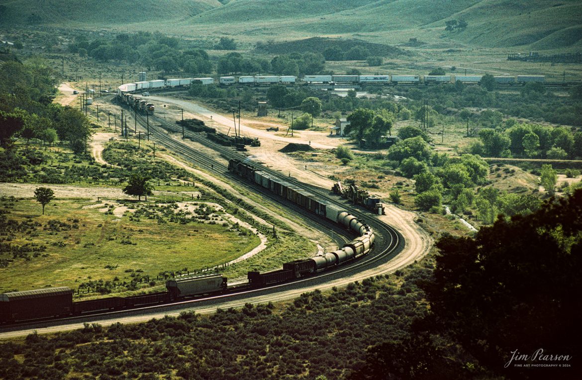 Two trains meet at the location known as Caliente, which is north of Bakersfield, California in the Tehachapi mountains sometime in the early 1990 in this Kodachrome slide scan.

According to Wikipedia: Established in the 1870s, Caliente was originally named Allens Camp for a cattle rancher and settler named Gabriel Allen. Later, the name Agua Caliente, coming from hot springs in the area, was proposed and may have been used. This name conflicted with the community of the same name in Sonoma County. With the railroad's arrival in 1875, the shortened name Caliente was adopted.

Caliente prospered during Southern Pacific Railroad's construction of Tehachapi Pass line. For a time, the Telegraph Stage Line and the Cerro Gordo Freighting Co. also ran through Caliente and its full-time population grew to 200. There were approximately 60 buildings, including 20 or more saloons.

The Caliente post office opened in 1875, closed in 1883, and was re-established in 1890. The Caliente General Store was remodeled in 1980 to house the post office which is still in operation today.

The sound of diesel locomotives and railroad horns are present day and night. The community is along the track of the Union Pacific Railroad, Mojave Subdivision. The track loops around the post office as it winds through the local hills. Trains climb toward the Tehachapi summit eastbound or descend toward Bakersfield if westbound.

Tech Notes: Nikon F3 Film Camera, Nikon 800-200mm, f/stop and shutter speed not recorded

#railroad #railroads #train #trains #bestphoto #railroadengines #picturesoftrains #picturesofrailway #bestphotograph #photographyoftrains #trainphotography #JimPearsonPhotography