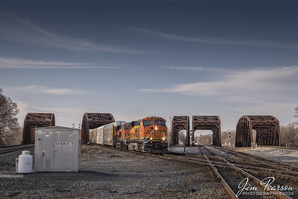 February 22, 2020 - BNSF 6347 leads an east bound autorack train through Blue Island Junction on the Indiana Harbor Belt line at Blue Island, Illinois.

From the web: One of the most fascinating rail hotspots anywhere, it's hard to know where to begin a description of it. Let's start by noting that Broadway crosses the entire maze approximately in the middle. Entering from the southeast is the double track CSX main line (owned by subsidiary Baltimore $amp; Ohio Chicago Terminal) coming from Barr Yard. Entering from the south and running alongside CSX for a short distance is the double track Indiana Harbor Belt line from Blue Island Yard. The CSX line then heads directly north into Chicago, while the IHB runs northwest for several miles before heading due north through the western suburbs of Chicago. There is an important crossover between the two lines just south of Broadway. Many CSX trains departing Barr Yard transfer to the IHB at this point, and the northwest line is best thought of as a joint IHB/CSX route (hereafter, the "joint line"). CSX's subsidiary B&OCT actually owns and maintains the track from here to a point a few miles south of LaGrange, Illinois, but IHB dispatches it and is otherwise responsible for its operation. From there north to the line's terminus at Franklin Park, Illinois, IHB owns the line outright.

Entering from the south and heading in a northerly direction into Chicago is the double track Canadian National (ex-Grand Trunk Western) mainline, which crosses the joint line just north of Broadway. Entering the junction from the southwest, and about 30 yards west of CN, is a single track line used by Iowa Interstate and once in a great while by CSX and Chicago Rail Link. This line extends north from the junction and feeds into the joint line. Trains using it sometimes back down the joint line to access Barr and Blue Island Yards. Between the CN and IAIS lines is a connector track, providing access to a small yard just south of the junction.

If the above were all there was, Blue Island would be a great place for trains. But there's more: at the south end of the plant, the Metra (ex-Rock Island) line crosses over the whole mess (Metra is the Chicago commuter train authority and they own the Rock Island tracks between Chicago and Joliet, Illinois). At the southwest corner of the junction, the IAIS track at the west end climbs up to connect with the Metra line.

Roughly 80-90 trains plow through the junction on a typical day, not counting the commuter trains and occasional freights on the overhead line. The joint line sees the most action, but the CSX main is busy as well. A small tower on Broadway in the middle of the junction once housed the crossing gates operator but was closed in 2013. The interlocking tower is at the far north end of the junction across the Calumet Sag Channel and is clearly visible from Broadway. However, it was shut down in June, 2013, and traffic is now handled remotely by CSX dispatchers. All of the tracks at the junction cross the channel on rugged, formidable truss bridges that look like they were built a thousand years ago (and are good for another thousand as well). The bridges on the north and the overhead Rock Island tracks on the south make Blue Island unique among busy junctions here or anywhere else.

More information: http://www.dhke.com/CRJ/blueisland.html