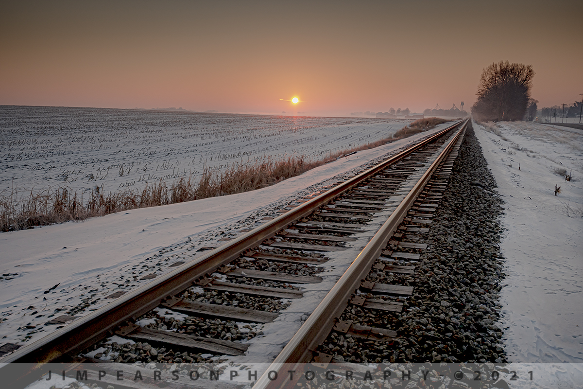 Morning sunrise on the Henderson Subdivision

I'm really not much of an early morning person unless I'm up to meet a friend to spend a day railfanning, but scenes like this have got me thinking I may get up early more often to catch the early morning and late evening light. I know it's there and it's golden it's just kinda hard to get up and out the door!!

On this day, February 19th, 2021, I was headed down to Guthrie, Ky to link up with fellow railfan Cooper Smith to spend a day railfanning the Henderson Subdivision in the snow.

I was watching this sunrise develop as I made my way south when I pulled over to a crossing just north of Trenton, Kentucky to catch this waiting on a train photo. It's not always about the train when you're trackside so always keep an eye out for other shots that might tell the story of railroading.

Tech Info: Nikon D800, RAW, Nikon 10-20mm DX lens @ 20mm f/4.5, 1/800, ISO 180 -0.7 Exp. Comp (helps with the highlights).