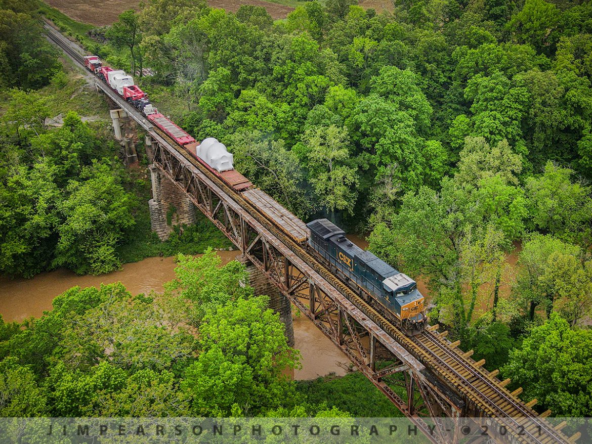 Southbound W992-28 High and Wide Move over the Red River at Adams, Tennessee

When you're running at 25 mph and only 5 mph through switches, it pretty much takes forever to get anywhere as with CSX W992-28 as it heads south across the Red River trestle at Adams, Tennessee on the CSX Henderson Subdivision with CSXT #9 leading on May 5th, 2021. It left Evansville, Indiana around midnight and ended up tying down at Courtland, TN where it covered 125 miles in about 12 hours.

Based on past moves this looks like another GE generator that is bound for Florida. Still trying to find out and will add it to the caption once I do.

This was an Emmert International train move with CSXT #9 as power and BBCX 1002 as the trailing manned caboose with what appeared to be a steam generator of some sort that was being hauled on their BBCX1000 Schnabel Railcar.

According to the Emmert International website: "Emmert International's BBCX1000 Schnabel Railcar is specifically designed to carry heavy (up to 1 million pounds) and oversized loads in such a way that the load itself makes up part of the car. The load is suspended between the two ends of the cars by lifting arms; the lifting arms are connected to a pivot above an assembly of pivots and frames that carry the weight of the load and the lifting arm."

For loads not designed to be part of the car Emmert International's BBCX1000 is equipped with a deck designed to carry the loads in standard configuration up to 836,000 pounds. Customized decks can be manufactured to increase the overall payload weight.

Emmert International's BBCX1000 is equipped with hydraulic equipment that will either lift the load vertically or horizontally shift the load while in transit to clear obstructions along the cars route.

With 20 axles (ten for each half) containing four trucks connected by a complex system of span bolsters its tare (unloaded) weight without deck is 424,000 lbs. The BBCX1000's empty car length is 115' 10" with a maximum length with the loading deck at 168' 9". Maximum vertical load shifting ability is 14" and the maximum horizontal load shifting ability is 22". The heavy-duty AAR railcar mechanical designation is LS.

Emmert Internationals BBCX1000 Schnabel Railcar is accompanied by the BBCX 1002 Caboose and BBCX1003 flat car that carries the deck when not in service. The 

BBCX1000 is pulled by special train service and requires 2 operators who control the BBCX 1000 railcar ride in the caboose.

I'll be posting a video on this move in a few days on my YouTube Channel and here on Facebook, once I get it edited.

Tech Info: DJI Mavic Air 2 Drone, RAW, 4.5mm (24mm equivalent lens) f/2.8, 1/320, ISO 200.