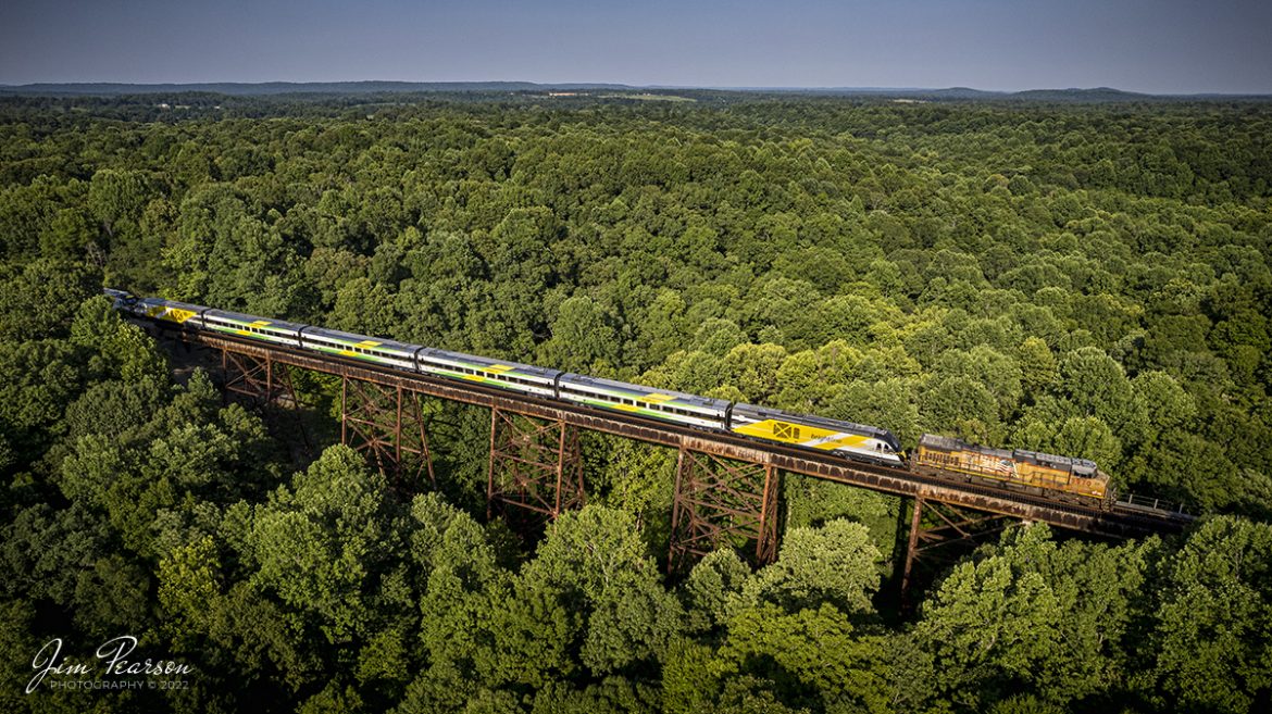 CSX S988 heads south over Gum Lick Trestle, just north of Kelly, Kentucky with two new Brightline Green and Pink commuter train sets, with UP 5970 leading, as they head for Florida, on the Henderson Subdivision on July 16th, 2022.

The Gum Lick name comes from the fact that the valley here is named Gum Lick Hollow and it sits between Crofton and Kelly Kentucky where it crosses over the West Fork of Pond River, and it is the highest trestle on the CSX Henderson Subdivision. 

These train sets were built by Siemens in Sacramento, California and are destined for service along Brightlines routes in Florida. 

According to Wikipedia: Brightline is a privately run inter-city rail route between Miami and West Palm Beach, Florida that runs on track owned by Florida East Coast Railway. An extension from West Palm Beach to Orlando International Airport is expected to open in 2023.

Brightline is the only privately owned and operated intercity passenger railroad in the United States. Its development started in March 2012 as All Aboard Florida by Florida East Coast Industries; a Florida real estate developer owned by Fortress Investment Group. Construction began in November 2014 and the route opened in January 2018.

Tech Info: DJI Mavic Air 2S Drone, RAW, 22mm, f/2.8, 1/1250, ISO 120.

#trainphotography #railroadphotography #trains #railways #dronephotography #trainphotographer #railroadphotographer #jimpearsonphotography