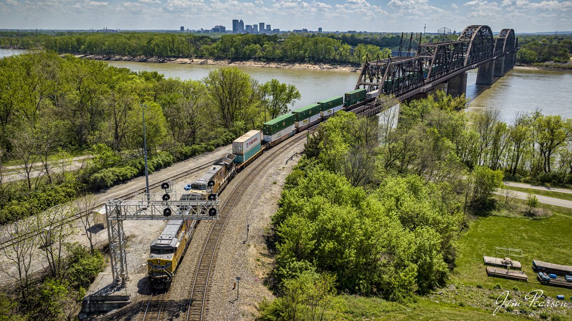 Union Pacific 6808 and 2659 lead Norfolk Southern 224 off the K&I bridge out of Louisville, Kentucky as they head west over the Ohio River into New Albany, Indiana on the NS Southern East District on April 15th, 2023.

According to Wikipedia: The Kentucky & Indiana Bridge is one of the first multi modal bridges to cross the Ohio River. It is for both railway and common roadway purposes together. By federal, state, and local law railway and streetcar, wagon-way, and pedestrian modes of travel were intended by the City of New Albany, City of Louisville, State of Kentucky, State of Indiana, the United States Congress, and the bridge owners. 

The K & I Bridge connects Louisville, Kentucky to New Albany, Indiana. Constructed from 1881 to 1885 by the Kentucky and Indiana Bridge Company, the original K&I Bridge opened in 1886. It included a single standard gauge track and two wagon ways, allowing wagons and other animal powered vehicles to cross the Ohio River by a method other than ferry for the first time. At the time motorized vehicles were virtually nonexistent. 

The K&I Bridge company also owned a ferry boat operation during both the 1st and 2nd bridge; eventually that operation was sold as the bridge's success largely outmoded boat usage.

In 1910 the bridge company was renamed the Kentucky & Indiana Terminal Railroad Co. From 1910 to 1912, a new, heavier bridge was built on new piers just upstream from the original one, after which the old bridge was demolished. The new bridge was double tracked to handle increasingly heavier train and now automobile traffic, eventually receiving the U.S. 31W designation.

The bridge also featured a rotating swing span opening for the passage of ships in high water. The bridge was only opened four times, twice for testing in 1913 and 1915, then in 1916 for the passage of the steamer "Tarascon" and in 1920 for passage of the Australian convict ship "Success". In 1948 it refused opening of the span for passage of the steamer "Gordon C. Greene" citing inconvenience and costs of cutting power and communication lines, an action for which K&I and LG&E both paid damages to that ship's company. In 1955 the K&I sought and received permission to permanently tie down the swing span from the Corps of Engineers. In 1952, the creosoted wood block roadways of the second bridge were eliminated and replaced by a steel gridwork roadway.

On February 1, 1979, an overweight dump truck caused a small segment of the steel grate roadway on the bridge to sag about 1 foot (0.30 m). A quick survey promised to reopen the roadway, but automotive traffic was banned thereafter by the railroad.

Tech Info: DJI Mavic 3 Classic Drone, RAW, 24mm, f/2.8, 1/2500 sec, ISO 140.

#trainphotography #railroadphotography #trains #railways #dronephotography #trainphotographer #railroadphotographer #jimpearsonphotography #kentuckytrains #mavic3classic #drones #trainsfromtheair #trainsfromadrone #KandIbridge #LouisvilleKy #NSsoutherneast #norfolksouthern