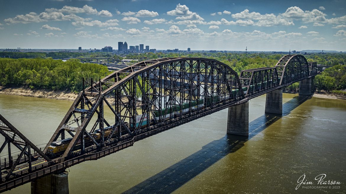 Union Pacific 6808 and 2659 lead Norfolk Southern 224 across the K&I bridge out of Louisville, Kentucky as they head west over the Ohio River into New Albany, Indiana on the NS Southern East District on April 15th, 2023, with downtown Louisville, Ky in the background.

According to Wikipedia: The Kentucky & Indiana Bridge is one of the first multi modal bridges to cross the Ohio River. It is for both railway and common roadway purposes together. By federal, state, and local law railway and streetcar, wagon-way, and pedestrian modes of travel were intended by the City of New Albany, City of Louisville, State of Kentucky, State of Indiana, the United States Congress, and the bridge owners. 

The K & I Bridge connects Louisville, Kentucky to New Albany, Indiana. Constructed from 1881 to 1885 by the Kentucky and Indiana Bridge Company, the original K&I Bridge opened in 1886. It included a single standard gauge track and two wagon ways, allowing wagons and other animal powered vehicles to cross the Ohio River by a method other than ferry for the first time. At the time motorized vehicles were virtually nonexistent. 

The K&I Bridge company also owned a ferry boat operation during both the 1st and 2nd bridge; eventually that operation was sold as the bridge's success largely outmoded boat usage.

In 1910 the bridge company was renamed the Kentucky & Indiana Terminal Railroad Co. From 1910 to 1912, a new, heavier bridge was built on new piers just upstream from the original one, after which the old bridge was demolished. The new bridge was double tracked to handle increasingly heavier train and now automobile traffic, eventually receiving the U.S. 31W designation.

The bridge also featured a rotating swing span opening for the passage of ships in high water. The bridge was only opened four times, twice for testing in 1913 and 1915, then in 1916 for the passage of the steamer "Tarascon" and in 1920 for passage of the Australian convict ship "Success". In 1948 it refused opening of the span for passage of the steamer "Gordon C. Greene" citing inconvenience and costs of cutting power and communication lines, an action for which K&I and LG&E both paid damages to that ship's company. In 1955 the K&I sought and received permission to permanently tie down the swing span from the Corps of Engineers. In 1952, the creosoted wood block roadways of the second bridge were eliminated and replaced by a steel gridwork roadway.

On February 1, 1979, an overweight dump truck caused a small segment of the steel grate roadway on the bridge to sag about 1 foot (0.30 m). A quick survey promised to reopen the roadway, but automotive traffic was banned thereafter by the railroad.

Tech Info: DJI Mavic 3 Classic Drone, RAW, 24mm, f/2.8, 1/2500 sec, ISO 120.

#trainphotography #railroadphotography #trains #railways #dronephotography #trainphotographer #railroadphotographer #jimpearsonphotography #kentuckytrains #mavic3classic #drones #trainsfromtheair #trainsfromadrone #KandIbridge #LouisvilleKy #NSsoutherneast #norfolksouthern