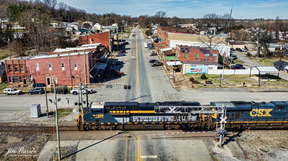 CSX Chesapeake & Ohio Heritage unit 1869 leads hot intermodal, CSX I025, as it passes through the crossing on Main Street in Sebree, Kentucky headed south on the Henderson Subdivision on February 29th, 2024.

According to the CSX Website: A locomotive commemorating the proud history of the Chesapeake and Ohio Railway has entered service as the fifth in the CSX heritage series celebrating the lines that came together to form the modern railroad.

Numbered CSX 1869 in honor of the year the C&O was formed in Virginia from several smaller railroads, the newest heritage locomotive sports a custom paint design that includes today’s CSX colors on the front of the engine and transitions to a paint scheme inspired by 1960s era C&O locomotives on the rear two-thirds.

The C&O Railway was a major line among North American freight and passenger railroads for nearly a century before becoming part of the Chessie System in 1972 and eventually merging into the modern CSX. In 1970, the C&O included more than 5,000 route miles of track stretching from Newport News, Virginia, to Chicago and the Great Lakes.

Designed and painted at CSX’s locomotive shop in Waycross, Georgia, the C&O unit will join four other commemorative units in revenue service on CSX’s 20,000-mile rail network.

The heritage series is reinforcing employee pride in the history of the railroad that continues to move the nation’s economy with safe, reliable, and sustainable rail-based transportation services.

Tech Info: DJI Mavic 3 Classic Drone, RAW, 22mm, f/2.8, 1/2500, ISO 100.

#trainphotography #railroadphotography #trains #railways #jimpearsonphotography #trainphotographer #railroadphotographer #csxt #dronephoto #trainsfromadrone #trending #CSXHeritageUnit