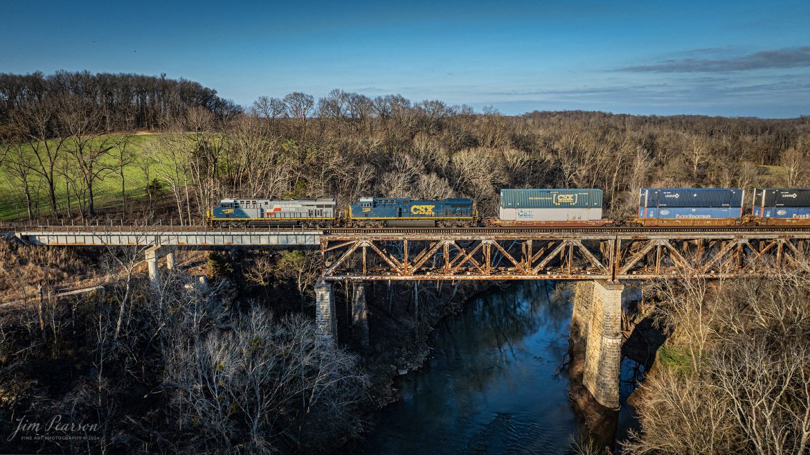 CSX Heritage series locomotive 1982, the Seaboard System unit, heads north across the Red River Bridge at Adams, Tennessee, as it leads CSX I026 northbound on the Henderson Subdivision on March 2nd, 2024.

According to Wikipedia: The Seaboard System Railroad, Inc. (reporting mark SBD) was a US Class I railroad that operated from 1982 to 1986.

Since the late 1960s, Seaboard Coast Line Industries had operated the Seaboard Coast Line and its sister railroads notably the Louisville & Nashville and Clinchfield as the “Family Lines System”. In 1980, SCLI merged with the Chessie System to create the holding company CSX Corporation; two years later, CSX merged with the Family Lines railroads to create the Seaboard System Railroad.

In 1986, Seaboard renamed itself CSX Transportation, which absorbed the Chessie System’s two major railroads the following year.

Tech Info: DJI Mavic 3 Classic Drone, RAW, 24mm, f/2.8, 1/1250, ISO 180.
#trainphotography #railroadphotography #trains #railways #jimpearsonphotography #trainphotographer #railroadphotographer #dronephoto #trainsfromadrone #TennesseeTrains #trending