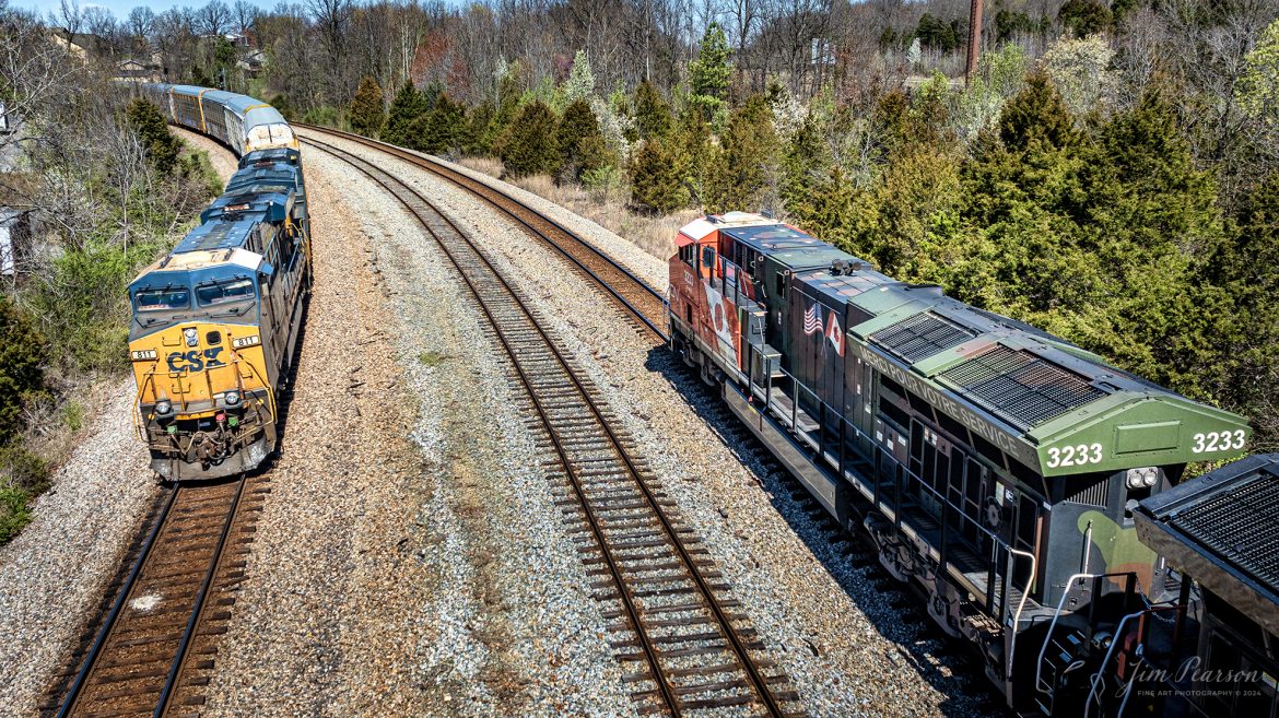 Canadian National (CN) locomotive 3233 (Support our Troops) leads B229-13 as they wait for hot intermodal I025 to pass at Arklow, at Madisonville, Kentucky, on the CSX Henderson Subdivision, March 16th, 2024, so they can continue their move north.

From a CN Press Release: “CN’s two tribute locomotives (CN 3233 & 3015) pay homage to veterans and active military men and women across North America. Their custom design represents the proud footprint we have established across our network and our deep recognition for the veterans who live and work in the communities our trains pass through every day. 

Tech Info: DJI Mavic 3 Classic Drone, RAW, 22mm, f/2.8, 1/1600, ISO 100.

#trainphotography #railroadphotography #trains #railways #jimpearsonphotography #trainphotographer #railroadphotographer #csxt #dronephoto #trainsfromadrone #trending #csxhendersonsubdivision #cnrailway