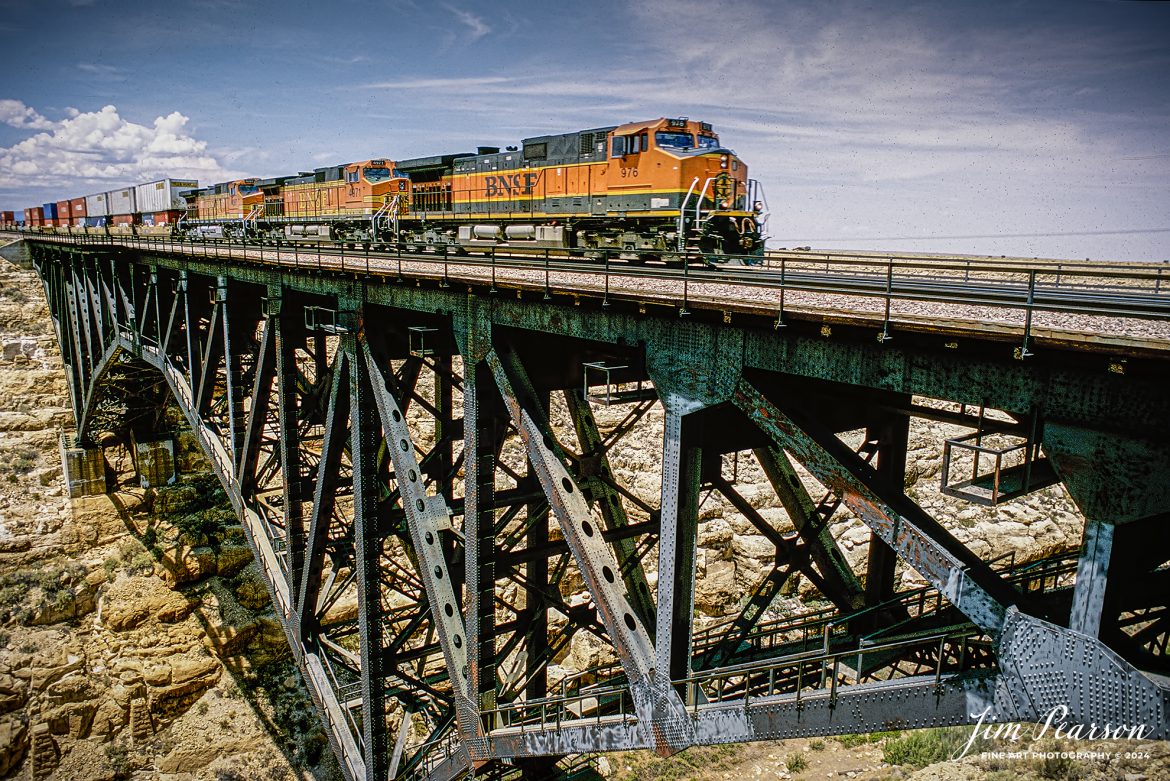 BNSF 976 leads a intermodal across the bridge at Diablo Canyon, Arizona as they head east on the BNSF Seligman Subdivision, through the Navajo Reservation in north central Arizona. From what I recall this slide was shot in the mid-1990s.

According to Wikipedia: Canyon Diablo is a ghost town in Coconino County, Arizona, United States on the edge of the arroyo Canyon Diablo. The community was settled in 1880 and died out in the early 20th century.

The ramshackle camp of railroad workers originated in 1880, due to the construction of the Atlantic and Pacific Railroad bridge over a large canyon named Canyon Diablo. The temporary community assumed the name of the canyon that stood in the way of the railroad construction - Canyon Diablo. The bridge construction took six months, during which many regular railroad construction workers were encamped and waiting to recommence their work once the canyon had been spanned. After the bridge was completed, construction resumed and the camp was largely abandoned.

When the railroad bridge was completed, the town quickly died. The original railroad bridge was replaced in 1900 with a new bridge to carry heavier locomotives and cars. By 1903, the only thing remaining in the town was a Navajo trading post. A new double track railroad bridge was completed across the Canyon in 1947. What remains today at Canyon Diablo are a few building foundations, the grave marker and grave of Herman Wolfe, the ruins of the trading post, a railroad siding and a double track railroad bridge.

Tech Notes: Nikon F3 Film Camera, Nikon 70-300mm lens at 200mm, f/stop and shutter speed not recorded

#railroad #railroads #train #trains #bestphoto #railroadengines #picturesoftrains #picturesofrailway #bestphotograph #photographyoftrains #trainphotography #JimPearsonPhotography