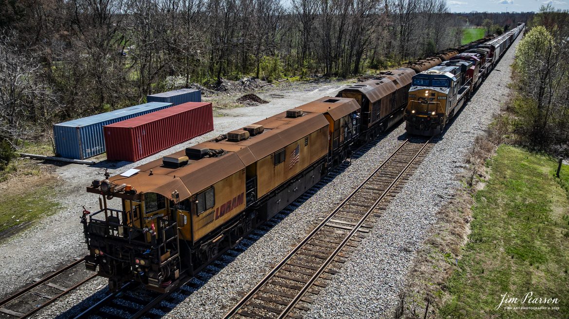 LORAM Railgrinder 305 waits in the siding at Crofton, Kentucky as they wait on B211 to clear so they can continue to grind their way south on March 24th, 2025, on the CSX Henderson Subdivision. 

According to Wikipedia: A railgrinder (or rail grinder) is a maintenance of way vehicle or train used to restore the profile and remove irregularities from worn tracks to extend its life and to improve the ride of trains using the track. Rail grinders were developed to increase the lifespan of the tracks being serviced for rail corrugation. Rail grinding is a process that is done to stop deformation due to use and friction on railroad tracks by removing deformations and corrosion.

Railroad tracks that experience continual use are more likely to experience corrugation and overall wear. Rail grinders are used to grind the tracks when rail corrugation is present, or before corrugation begins to form on the tracks. Major freight train tracks use rail grinders for track maintenance based on the interval of tonnage, rather than time.

Transit systems and subways in major cities continue to use scheduled rail grinding processes to combat the corrugation common to heavily used tracks. Rail-grinding equipment may be mounted on a single self-propelled vehicle or on a dedicated rail-grinding train which, when used on an extensive network, may include crew quarters. The grinding wheels, of which there may be more than 100, are set at controlled angles to restore the track to its correct profile.

Tech Info: DJI Mavic 3 Classic Drone, RAW, 22mm, f/2.8, 1/2000, ISO 140.

#railroad #railroads #train, #trains #railway #railway #railtransport #railroadengines #picturesoftrains #picturesofrailways #besttrainphotograph #bestphoto #photographyoftrains #bestsoldpicture #JimPearsonPhotography #trainsfromadrone #csxhendersonsubdivision #onecsx #loram #railgrinder