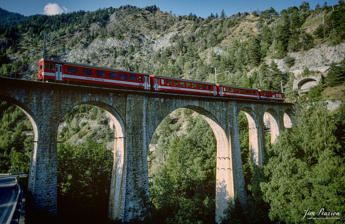 Film Wednesday – 1993 – Today’s slide scans are from a trip I took between Aviano, Italy and Zermatt, Switzerland. While at Zermatt I rented a car for the day and got out and about where I caught this shot of the Fuurka-Oberalp train on one of many viaducts in Switzerland. I haven’t a clue exactly to the location where this train set was at and again If anyone recognizes this location, let me know in the comments.

According to Wikipedia: The Furka Oberalp Railway (German: Furka Oberalp Bahn) is a narrow-gauge mountain railway in Switzerland with a gauge of 1,000 mm (3 ft 3+3⁄8 in). It runs in the Graubünden, Uri and Canton of Valais. Since January 1, 2003, it is part of the Matterhorn Gotthard Bahn when it merged with the BVZ Zermatt-Bahn.

The line begins in Disentis in the canton of Graubünden, where there is a connection to the Rhätische Bahn (RhB). It then runs over the Oberalp Pass to Andermatt in the canton of Uri. Through the Furka Base Tunnel, it reaches the Goms District area and Brig in the canton of Valais. In Brig, it connects to the BVZ Zermattbahn since 1930.

The first half of the line was opened by the French company Brig-Furka-Disentis Bahn (BFD) in 1914. Trains could go as far as Gletsch, starting from Brig. Construction of the second part over the Furka Pass and Oberalp Pass was well under way when the war situation in France halted all works by 1915. The company lingered on but was finally bankrupt in 1923. Two years later the railway had a new owner, called Furka Oberalp Bahn, founded by the cantons and the neighbouring railway companies. Construction work resumed, now with important federal funds, and on July 4, 1926, regular through services between Brig and Disentis could start. RhB trains reached Disentis under electric traction in 1922.

In 1930 the tracks of the newly electrified BVZ reached Brig, which gave birth to the famous Glacier Express. The oncoming crisis and the war limited the number of tourists. Nevertheless, the FO line was considered to be of strategic importance. This finally made funds available to electrify the line and purchase the necessary motive power. At the same time the Andermatt–Disentis line was protected against avalanches to allow winter services.

Tech Info: Camera, Nikon F3, Kodachrome Slide Film, no other data recorded, Scanned with a PlusTek 82001i Film Scanner.

#slidescan #filmphotography #trains #railroads #jimpearsonphotography #FilmPhotography