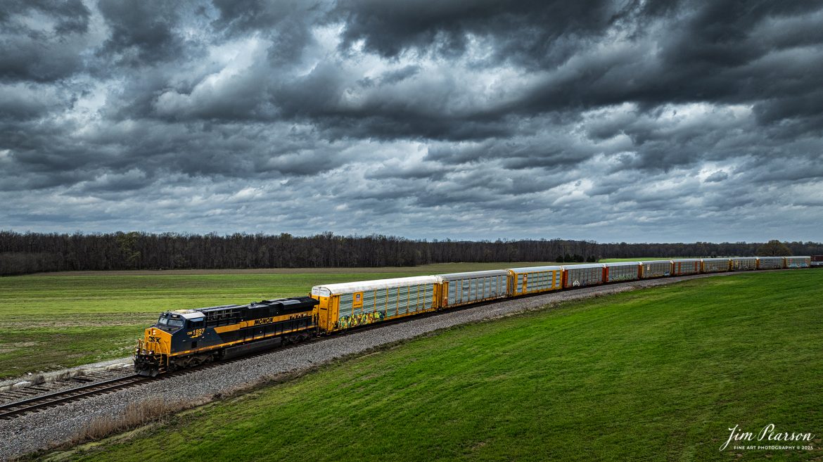 CSX I025 heads south at Breton, Kentucky as CSX Monon Heritage Unit 1897 leads it under dark threatening skies on April 2nd, 2025, on the CSX Henderson Subdivision. The eleven autoracks behind the engine are loaded with Tesla’s bound for Florida and overseas market from what I’m told.

Capturing this engine means I’ve caught all of CSX’s Heritage units except for the Georgia Heritage Unit, and that one is only a matter of time!

According to a CSX Press Release: January 26, 2024 - In a tribute to its rich railroad history, CSX has unveiled its Monon 1897 heritage locomotive, marking the ninth release its ongoing heritage series honoring the company's predecessor railroads.

“The Monon Railroad ran from Chicago down to Louisville but most of it was in Indiana,” explained CSX Carman Jason Merritt, who assisted with the heritage project. “Eventually it merged with the Louisville and Nashville Lines and was later absorbed by CSX.”

The new heritage locomotive emerges fresh from the Class I railroad's paint shop in Waycross, Ga., showcasing a blend of modern and historic aesthetics. The design features the modern CSX design on the head end, transitioning seamlessly into the historic paint scheme and logo of the Monon line. This style reflects the approach taken with previous installations in the CSX heritage series, which often feature the current CSX paint scheme on the nose and the predecessor's scheme on the body.

“A lot of hard work and planning goes into each project,” said Merritt. “We want to get these right, so we take pride in what we do, from the wash rack to moving them out the door.”

The new Monon heritage locomotive is a testament to the enduring legacy of America's railroads. It stands as a symbol of the past while simultaneously pointing towards the future, embodying the spirit of evolution and innovation that drives CSX.

Tech Info: DJI Mavic 3 Classic Drone, RAW, 22mm, f/2.8, 1/2000, ISO 130.

#railroad #railroads #train, #trains #railway #railway #railtransport #railroadengines #picturesoftrains #picturesofrailways #besttrainphotograph #bestphoto #photographyoftrains #bestsoldpicture #JimPearsonPhotography #trainsfromadrone #csxhendersonsubdivision #onecsx #csxheritageunit