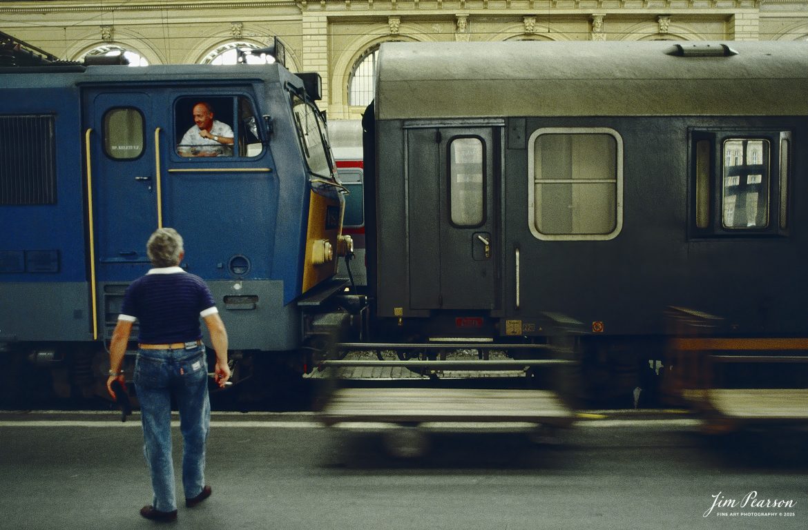 Film Wednesday – 1993 – Today’s slide scans are from time that I spent at the Budapest-Nyugati Railway Station, in Budapest, Hungry. This shot is of a engineer  chatting with other workers on the platform as a baggage cart passes, as they ready the train for departure.

According to Wikipedia, Budapest Nyugati station (Hungarian: Nyugati pályaudvar, pronounced [ˈɲuɡɒti ˈpaːjɒudvɒr]; lit. 'western railway station'), generally referred to simply as Nyugati, is one of the three main railway terminals in Budapest, Hungary. The station is on the Pest side of Budapest, accessible by the 4 and 6 tramline and the M3 metro line.

The station was designed by Auguste de Serres and was built by the Eiffel Company. It was opened on 28 October 1877. It replaced another station, which was the terminus of Hungary's first railway line, the Pest–Vác line (constructed in 1846). This building was demolished to construct the Grand Boulevard.

The station got its name from the adjacent Western Square ('Nyugati tér'), a major intersection where Teréz körút (Theresia Boulevard), Szent István körút (Saint Stephen Boulevard), Váci út (Váci Avenue), and Bajcsy-Zsilinszky út (Bajcsy-Zsilinszky Avenue) converge. The square also serves as a transport hub with several bus routes, tram routes 4 and 6, and a station on M3 of the Budapest Metro.

Beside the terminal and partially above its open area there is the WestEnd City Center shopping mall. Inside the station is a McDonald's restaurant which has been described as the "most elegant" McDonald's in the world.

The music video for Gwen Stefani's 2008 single Early Winter was partly shot at Nyugati. Starting in May 2016 the key scenes of the movie Terminal were shot over 27 nights.

Tech Info: Camera, Nikon F3, Ektachrome Slide Film, no other data recorded, Scanned with an PlusTek 82001i Film Scanner.

#slidescan #filmphotography #trains #railroads #jimpearsonphotography #FilmPhotography