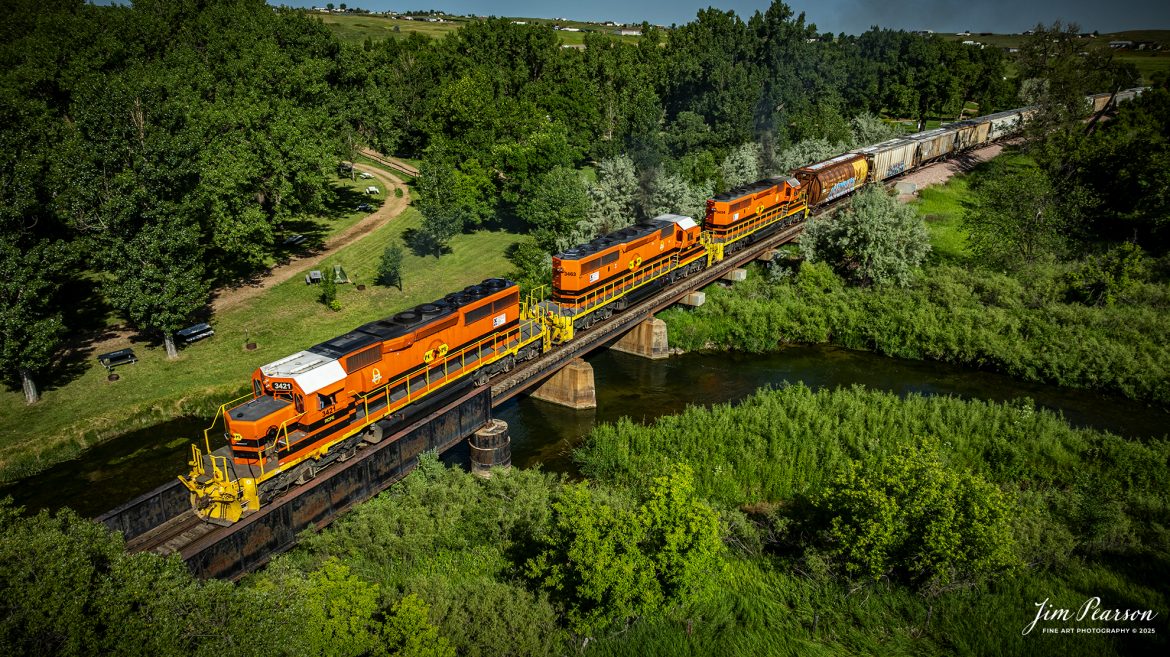Rapid City, Pierre & Eastern Railroad (RCPE) 3421 crosses the Redwater River as it leads their train eastbound out of Belle Fourche, as they head for Rapid City, South Dakota on the Black Hills Subdivision, on June 26th, 2025.

According to Wikipedia, the Rapid City, Pierre & Eastern Railroad (reporting mark RCPE) is a Class II freight railroad operating across South Dakota and southern Minnesota in the northern plains of the United States. Portions of the railroad also extend into Wyoming and Nebraska. It is owned and operated by Genesee & Wyoming. The primary commodities shipped are grain, clay, and cement. Operations began on June 1, 2014.

Genesee & Wyoming, a holding company of mostly short line railroads, formed the Rapid City, Pierre & Eastern to acquire the western end of the former Dakota, Minnesota and Eastern Railroad (DM&E) rail line from the Canadian Pacific Railway (CPR). The RCPE and DM&E entered an agreement on January 2, 2014, wherein RCPE would acquire 670 miles of track and 219 miles of trackage rights from the DM&E. The acquisition was completed on May 30, 2014, for $210 million. Most of its employees came from the DM&E.

Tech Info: DJI Mavic 3 Classic Drone, RAW, 24mm, f/5, 1/3200, ISO 100.

#railroad #railroads #train, #trains #railway #railway #steamtrains #railtransport #railroadengines #picturesoftrains #picturesofrailways #besttrainphotograph #bestphoto #photographyoftrains #bestsoldpicture #JimPearsonPhotography #trainsfromtheair #trainsfromadrone #rcperailway #shortlinerailroads #southdakotarailroads